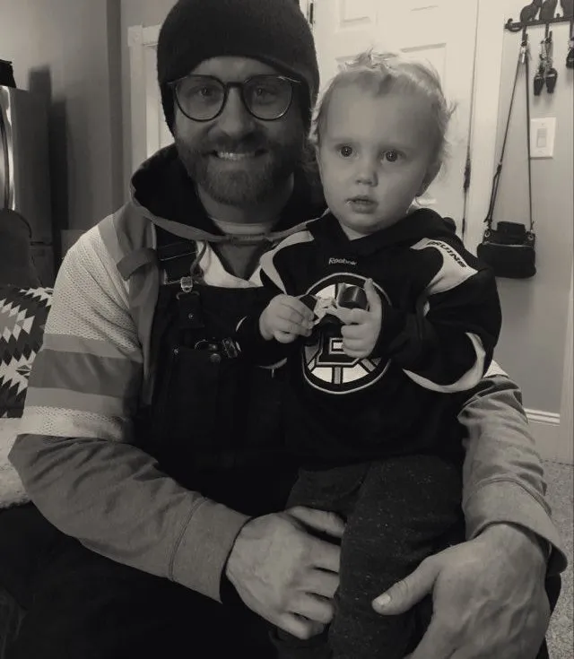 AJ McGeoch holding his young son, who is wearing a Boston Bruins jersey